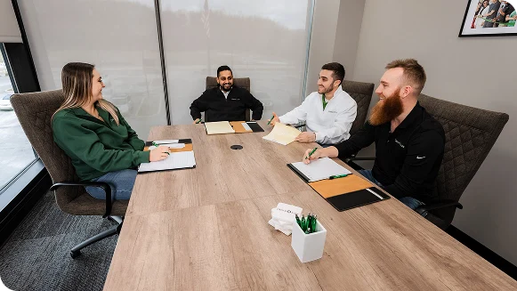 Three individuals seated at a conference table engaged in discussion within an office setting